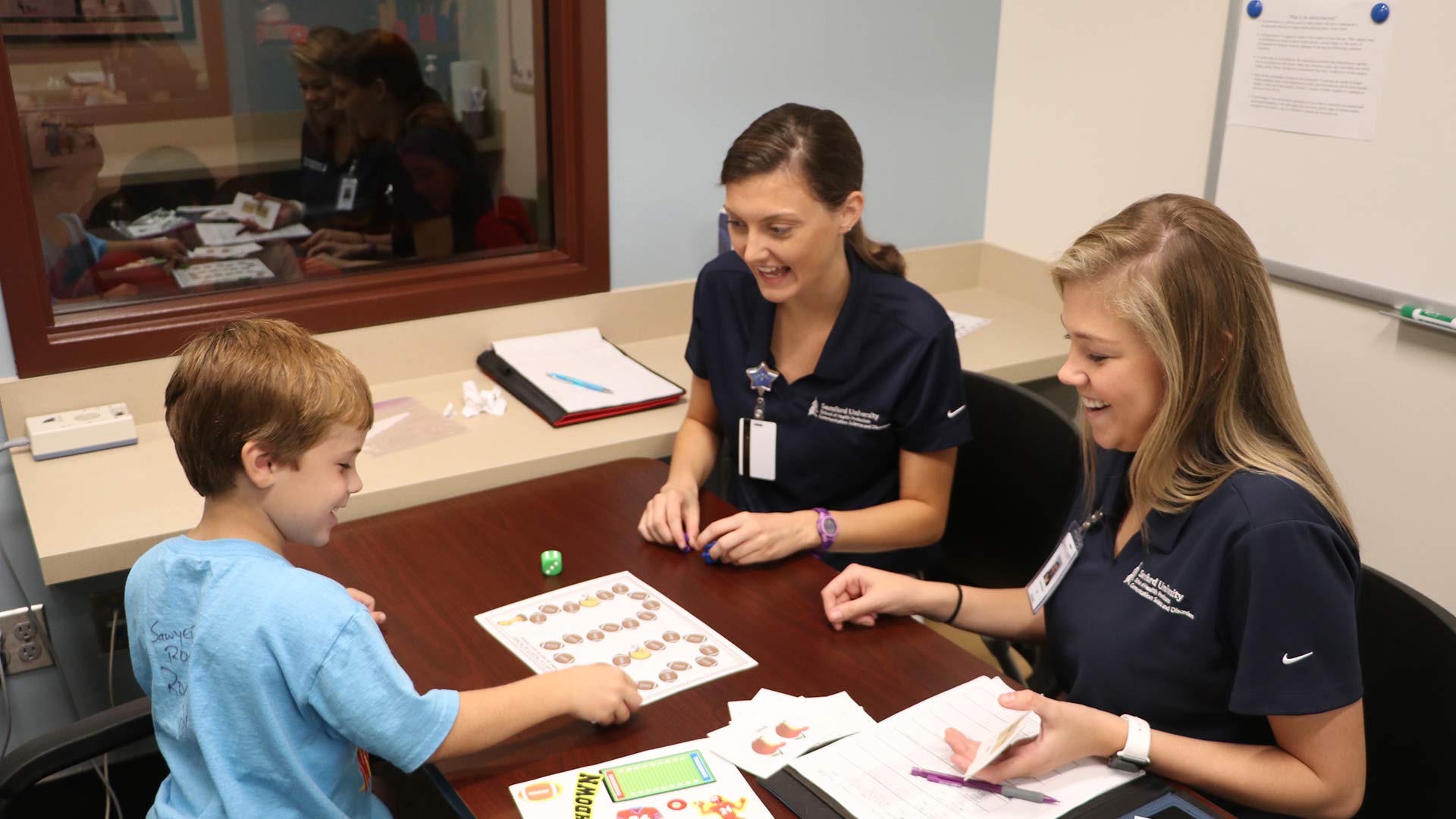 two female comm sci students teaching young boy