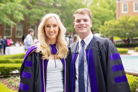 Male Student and Female Srudent Graduates Standing By Fountain